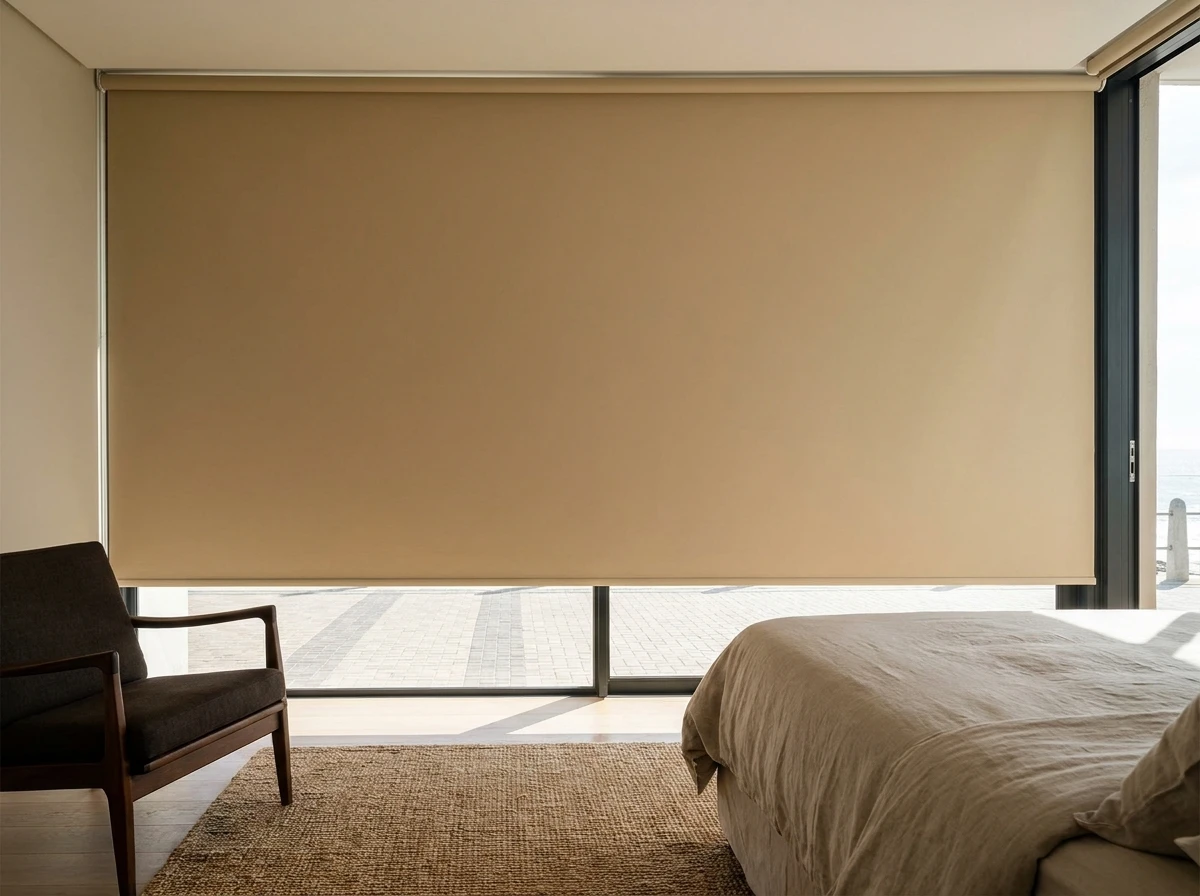 Blockout roller blind lowered in a Sea Point bedroom, with the promenade visible through the glass door